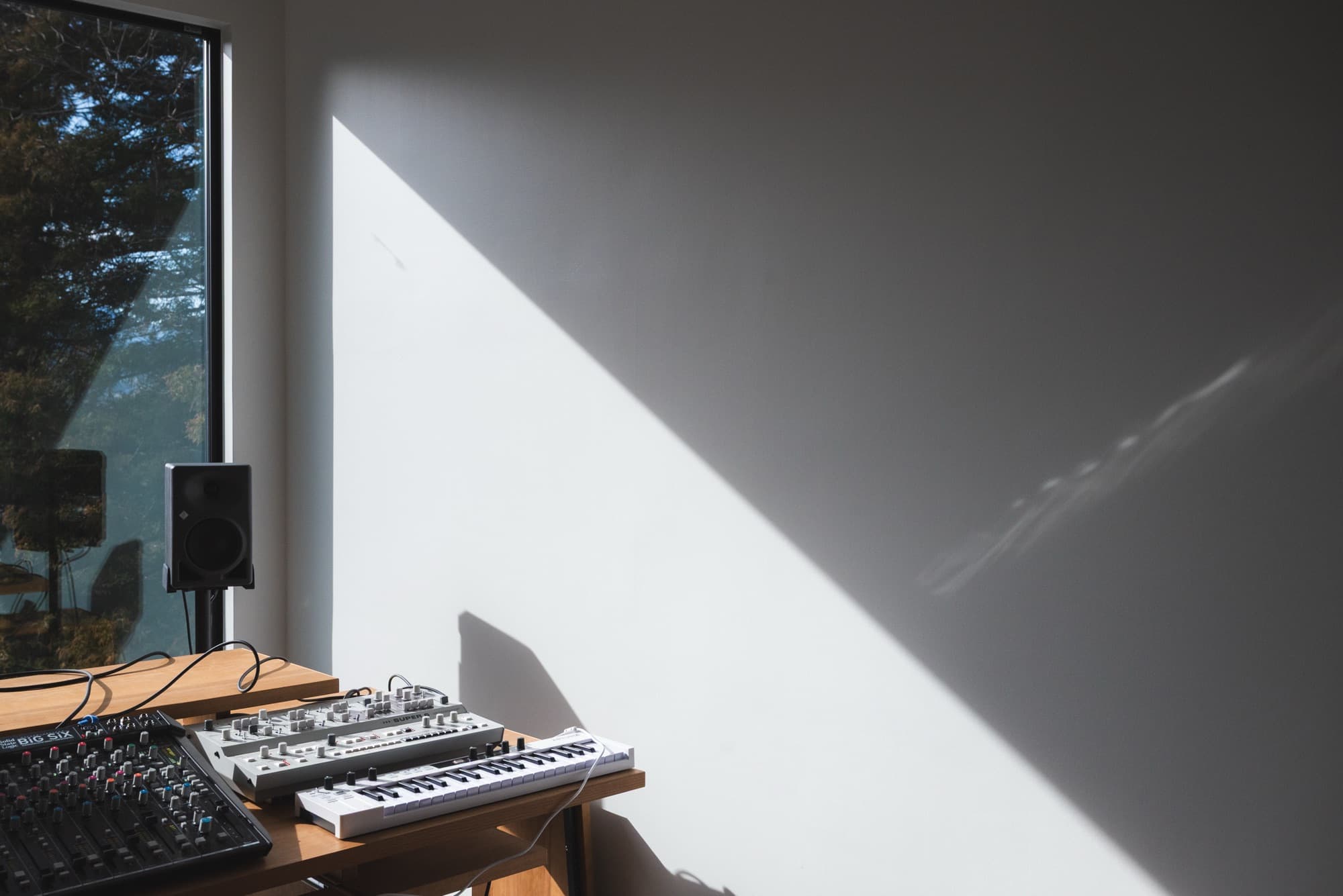 山並みを望む窓辺に SSL Big Six とシンセサイザーが並ぶ inou studio の室内